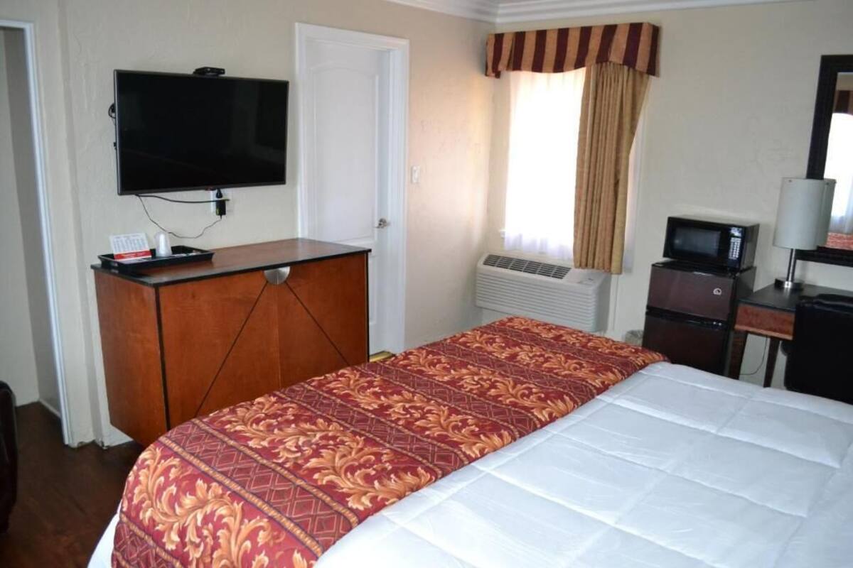 A hotel room with a bed, a television, a desk with a computer, and an air conditioning unit.