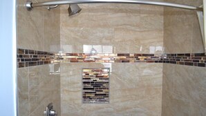 A shower with a glass door, a metal showerhead, and a tiled backsplash. - Rex Motel (Ventura)