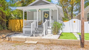 A white wooden house with a porch, a wooden fence, and a well-maintained lawn. - The P'Cola Sunrise. 1 bed 1 bath cottage (Pensacola)