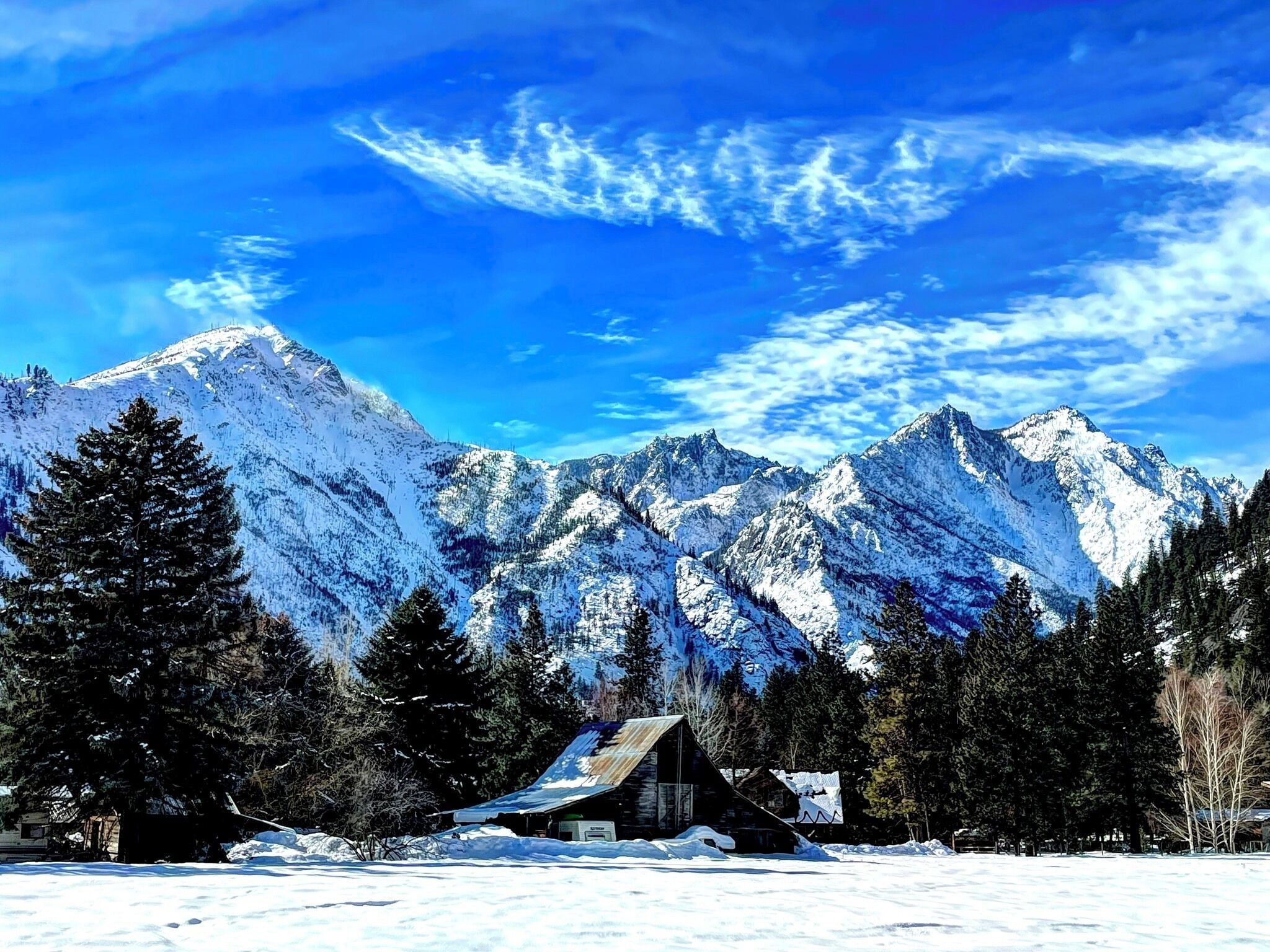 Una baita circondata da montagne innevate e alberi sempreverdi.