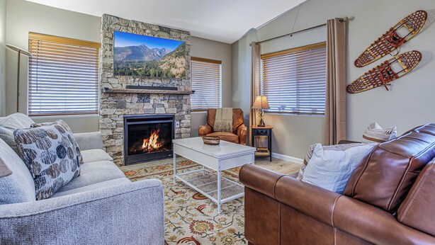 A living room with a stone fireplace, a television mounted above it, and a leather couch.