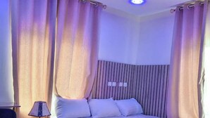 Un dormitorio con cama, mesita de noche con lámpara y cortinas.