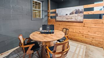 A round wooden table with four chairs, a black suitcase, and a framed picture on the wall.