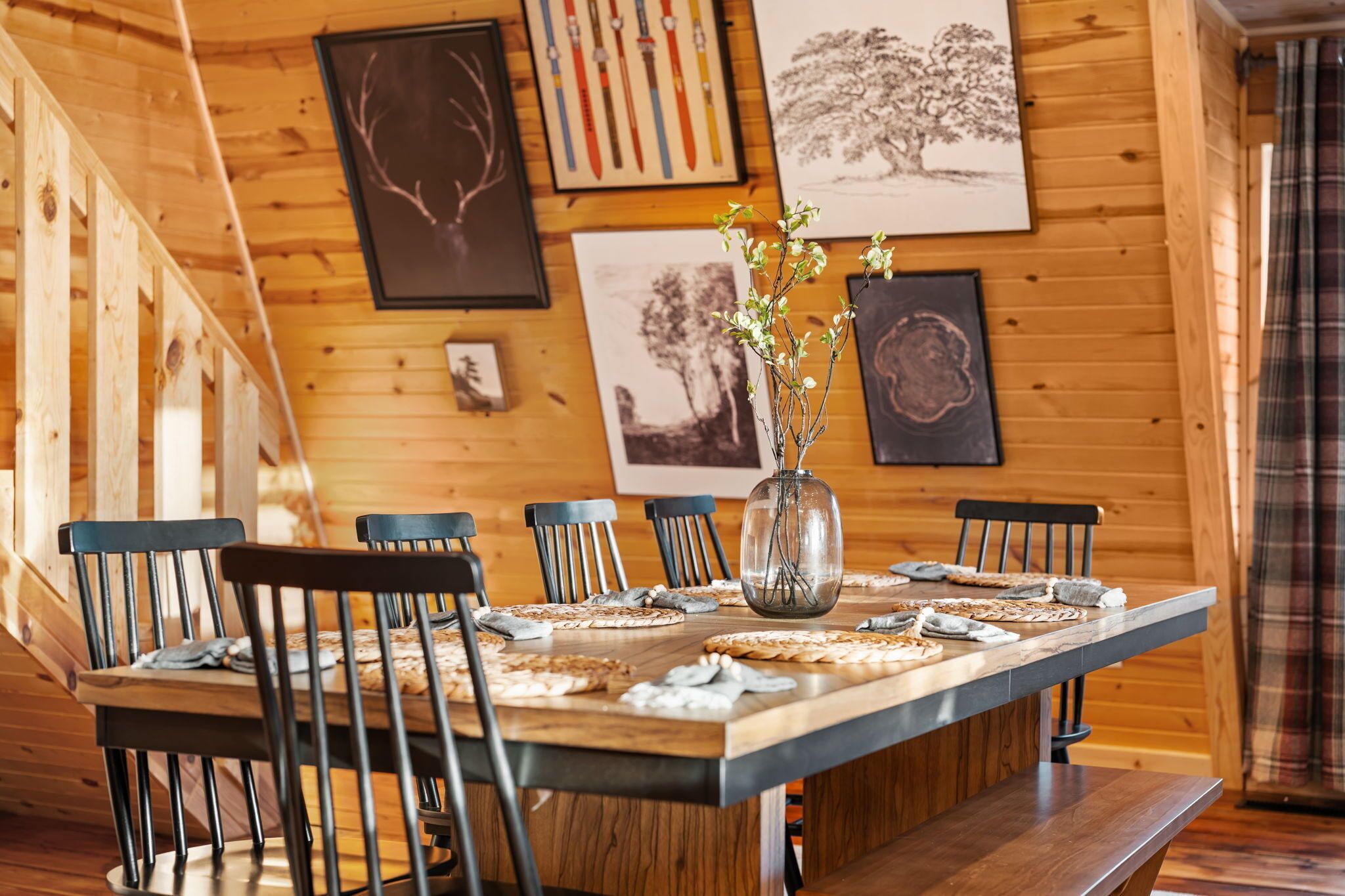 A wooden dining table with chairs, a vase with flowers, and framed artwork on the wall.