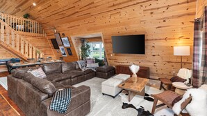 Ein großzügiges Wohnzimmer mit einem großen, braunen Ecksofa, einer Holztreppe und einem an der Wand befestigten Flachbildfernseher.