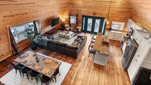 Ein geräumiger Loft-Raum mit Holzbalkendecke, einer gemütlichen Sitzecke mit Sofa und Sesseln, einem Esstisch mit Untertassen und einer Küchenzeile mit weißen Schränken und einem Kühlschrank.