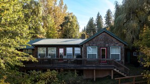A cabin with a deck, large windows, and a red door.