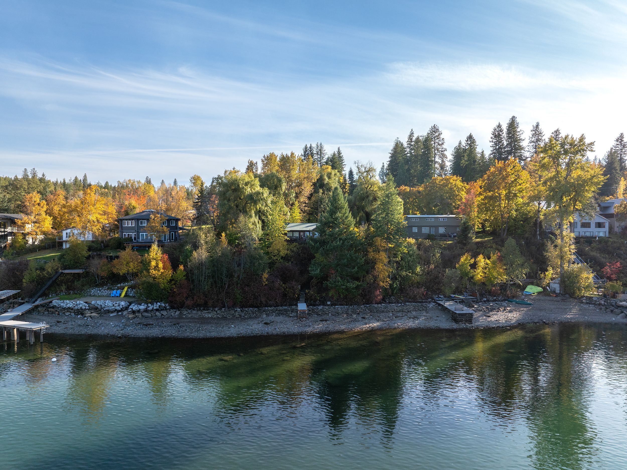 A lakeside residential area with houses surrounded by autumn foliage, a dock, and a calm water body.