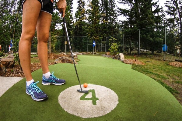 Una persona jugando minigolf sobre césped artificial verde, con un hoyo marcado '4'.
