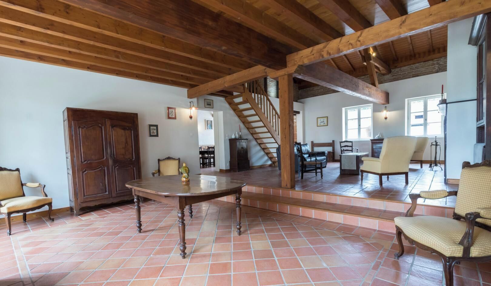 A spacious living area with a wooden dining table, comfortable seating, a staircase, and a view of the dining area.