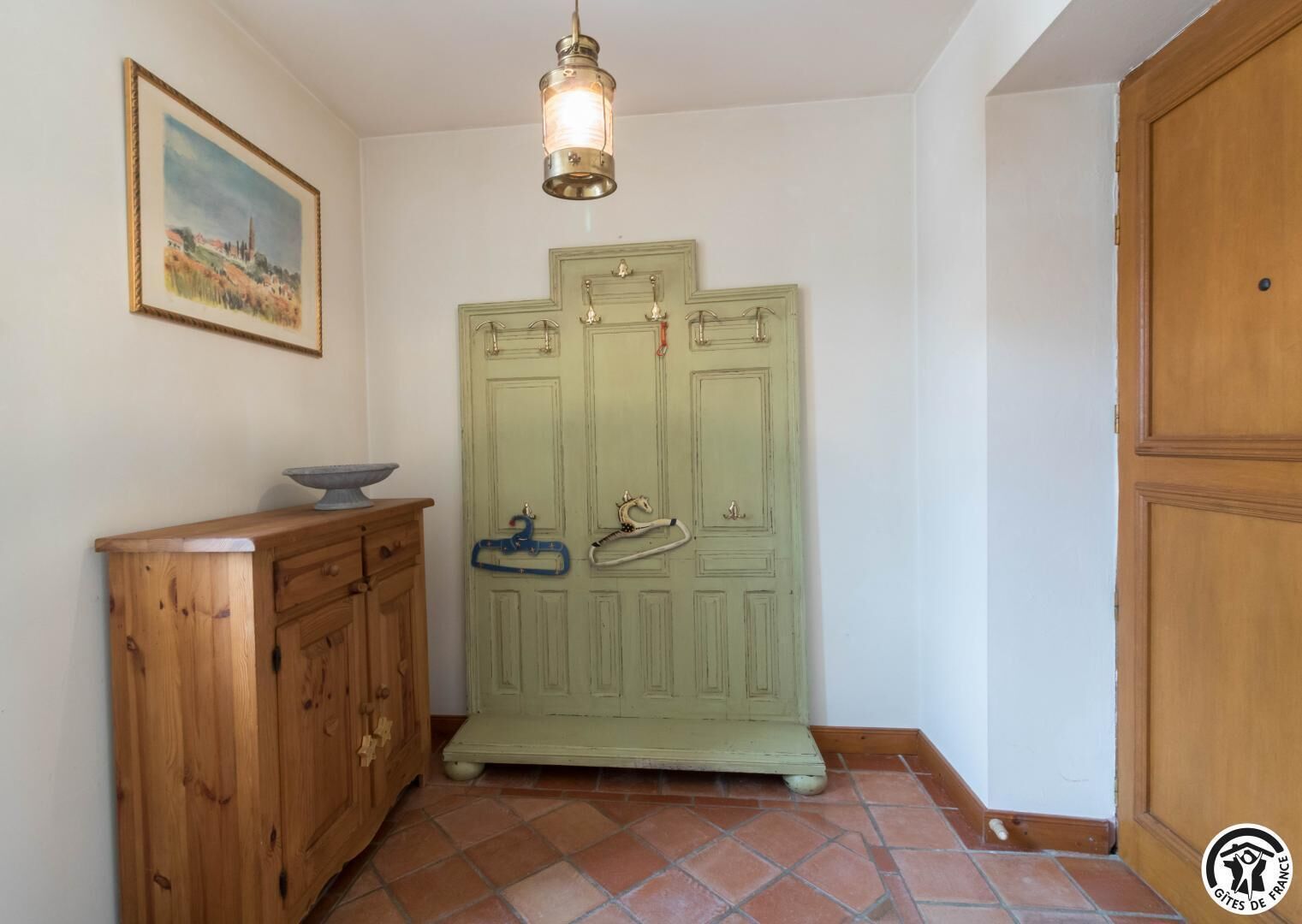 A room with a green wardrobe, a wooden cabinet, a hanging light fixture, and a framed picture on the wall.