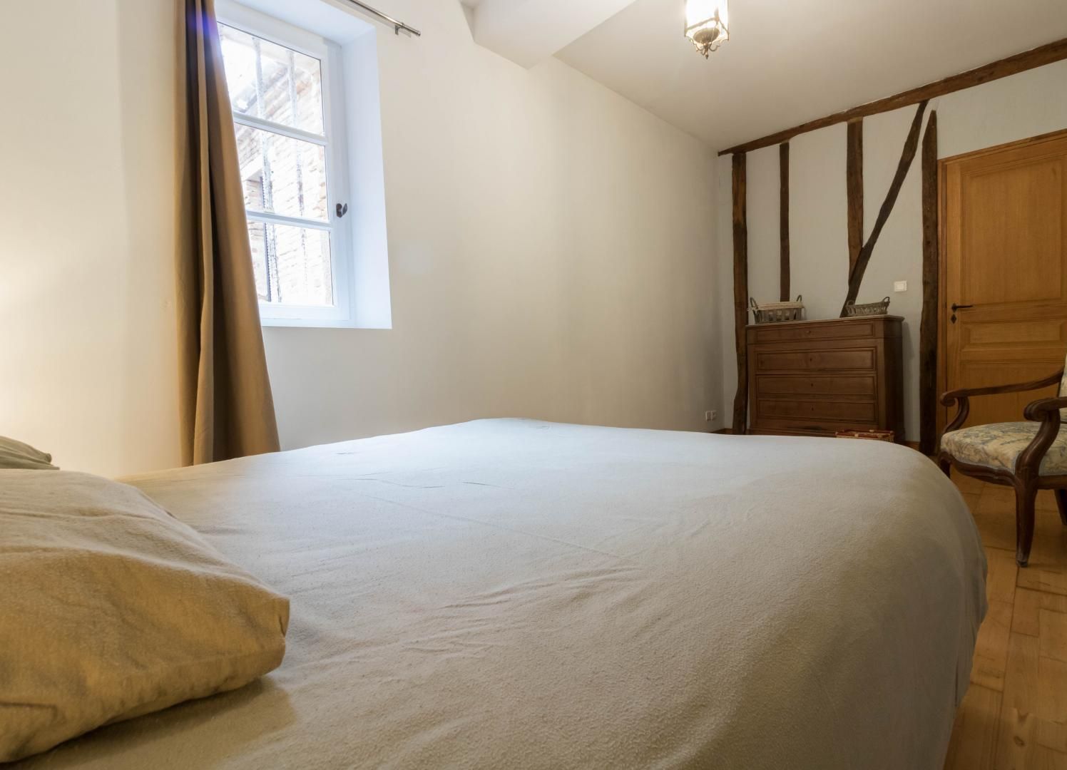 A bedroom with a large bed, a dresser, a chair, and a wardrobe.