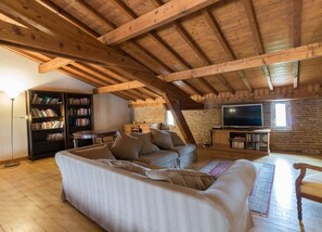 Un espacio tipo loft con vigas de madera a la vista, un sofá seccional, un televisor y estanterías.