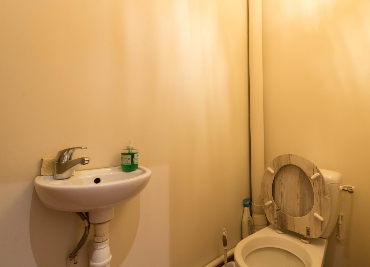 A bathroom with a sink, toilet, and a green bottle of hand soap.