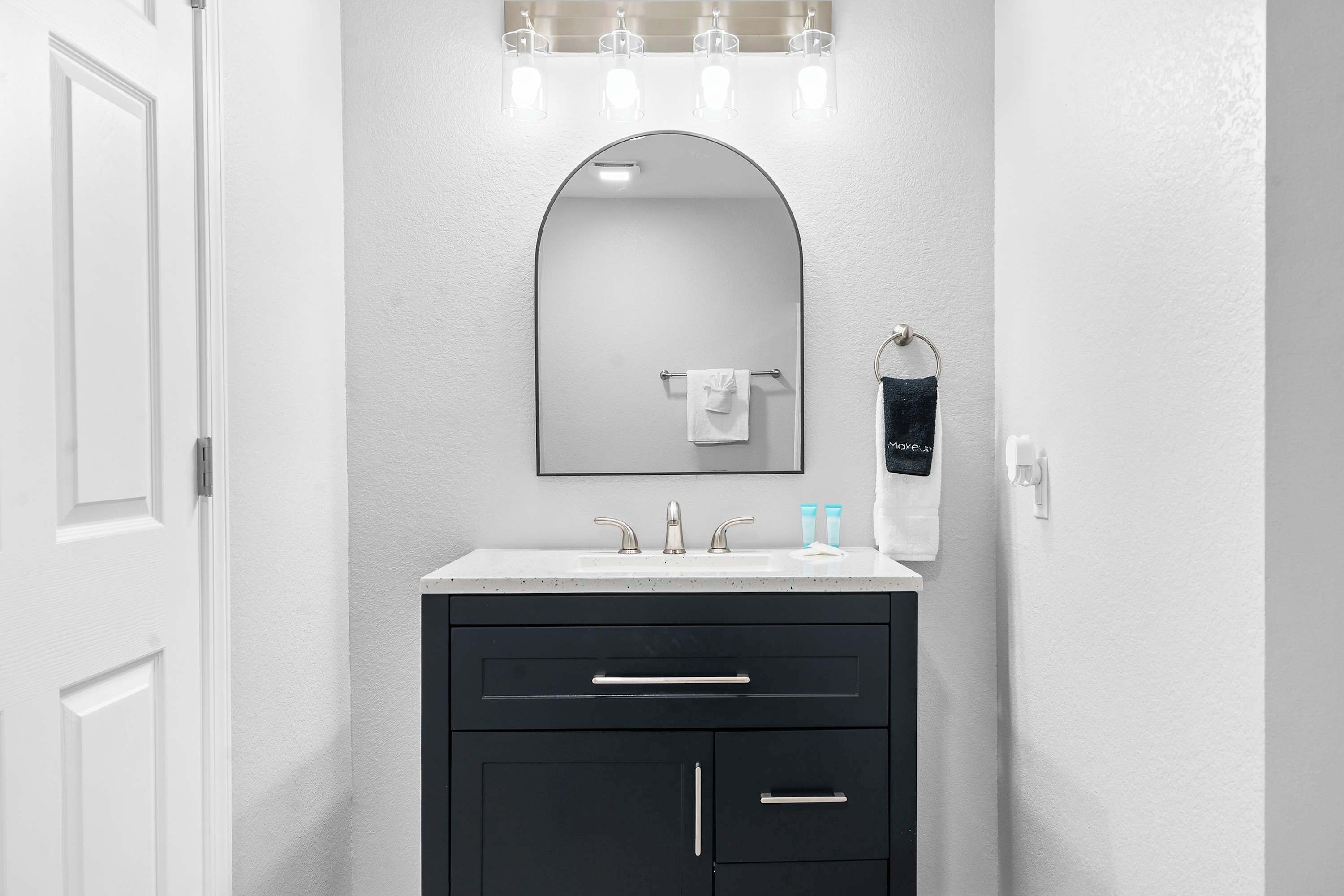 Une salle de bain avec un meuble-lavabo blanc, des armoires noires, un miroir et un porte-serviettes.