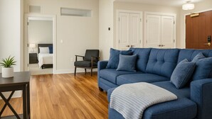 A living room with a blue sofa, a small table with a plant, and a wooden floor.