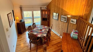 A dining area with a wooden table and chairs, a wooden cabinet, and a view of the outdoors through a window. - Marvelous 3-bedroom townhome in Hunter Mountain next to the slopes (Lanesville)