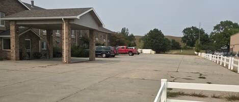 A parking lot with a covered area, a building with a brick facade, and a red truck parked in the distance.