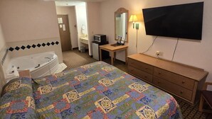 Ein Hotelzimmer mit Bett, Schreibtisch, Flachbildfernseher, Schreibtischlampe, Mikrowelle und einem Badezimmer mit Badewanne.