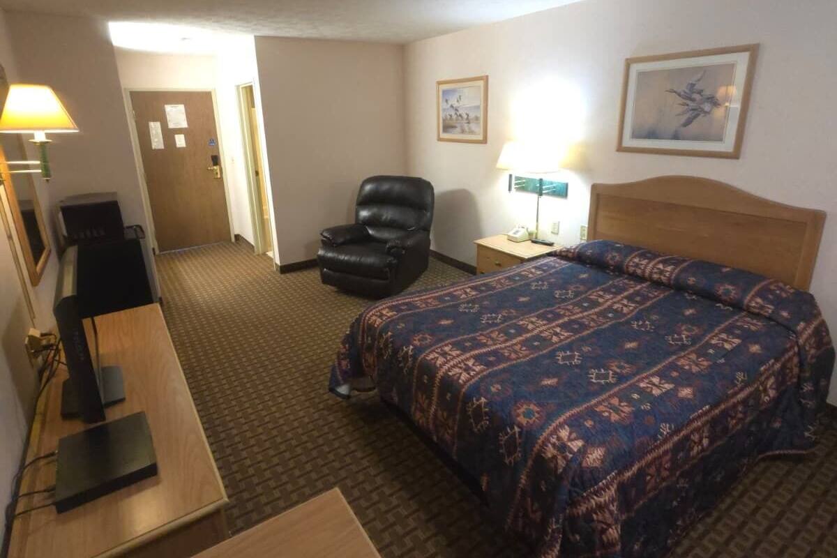 A hotel room with a bed, a desk, a chair, and a lamp.