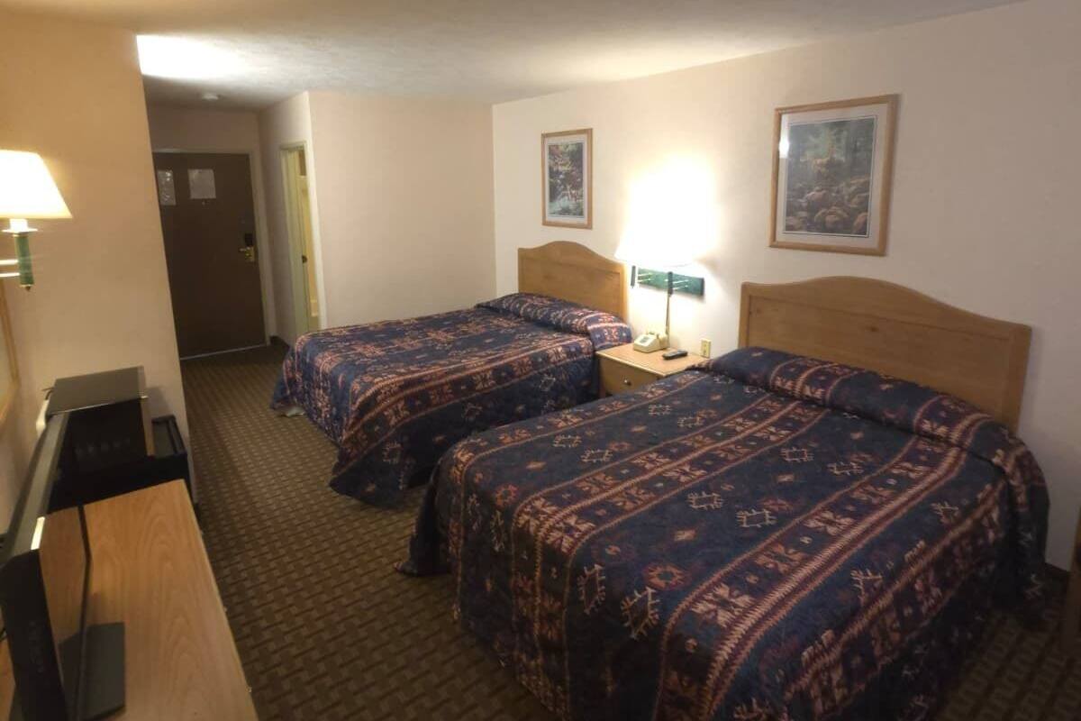 A hotel room with two beds, a desk, a chair, and a lamp.