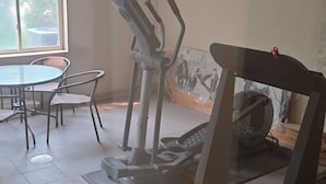 Ein Fitnessraum mit Trainingsgeräten, einem runden Tisch mit Stühlen und einem großen Fenster.