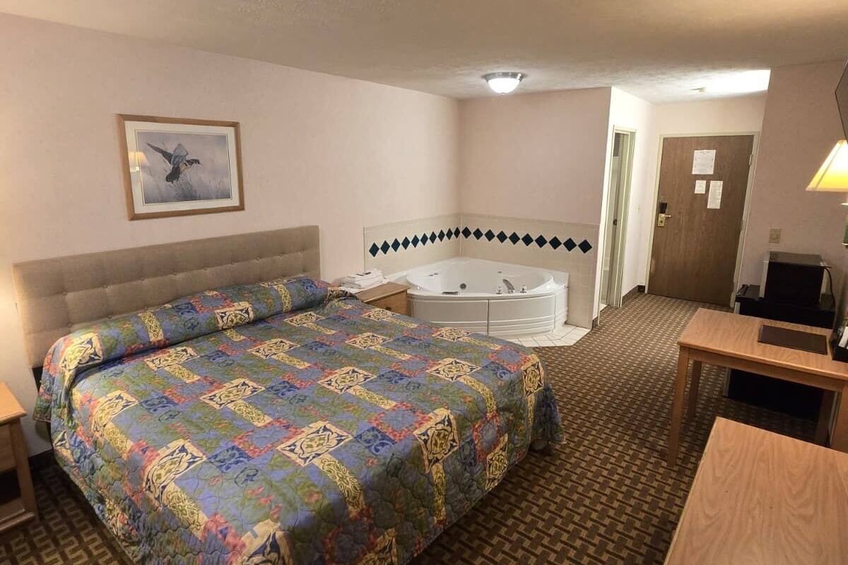 A hotel room with a large bed, a sitting area with a table, a bathtub, and a framed picture on the wall.
