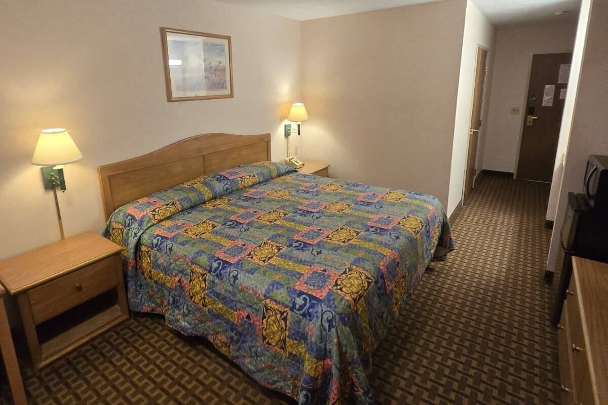 A hotel room with a large bed, two bedside lamps, a framed picture on the wall, and a patterned carpet.