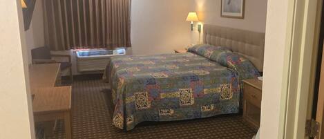 Una habitación de hotel con una cama, un escritorio, una silla, una lámpara y un cuadro en la pared.