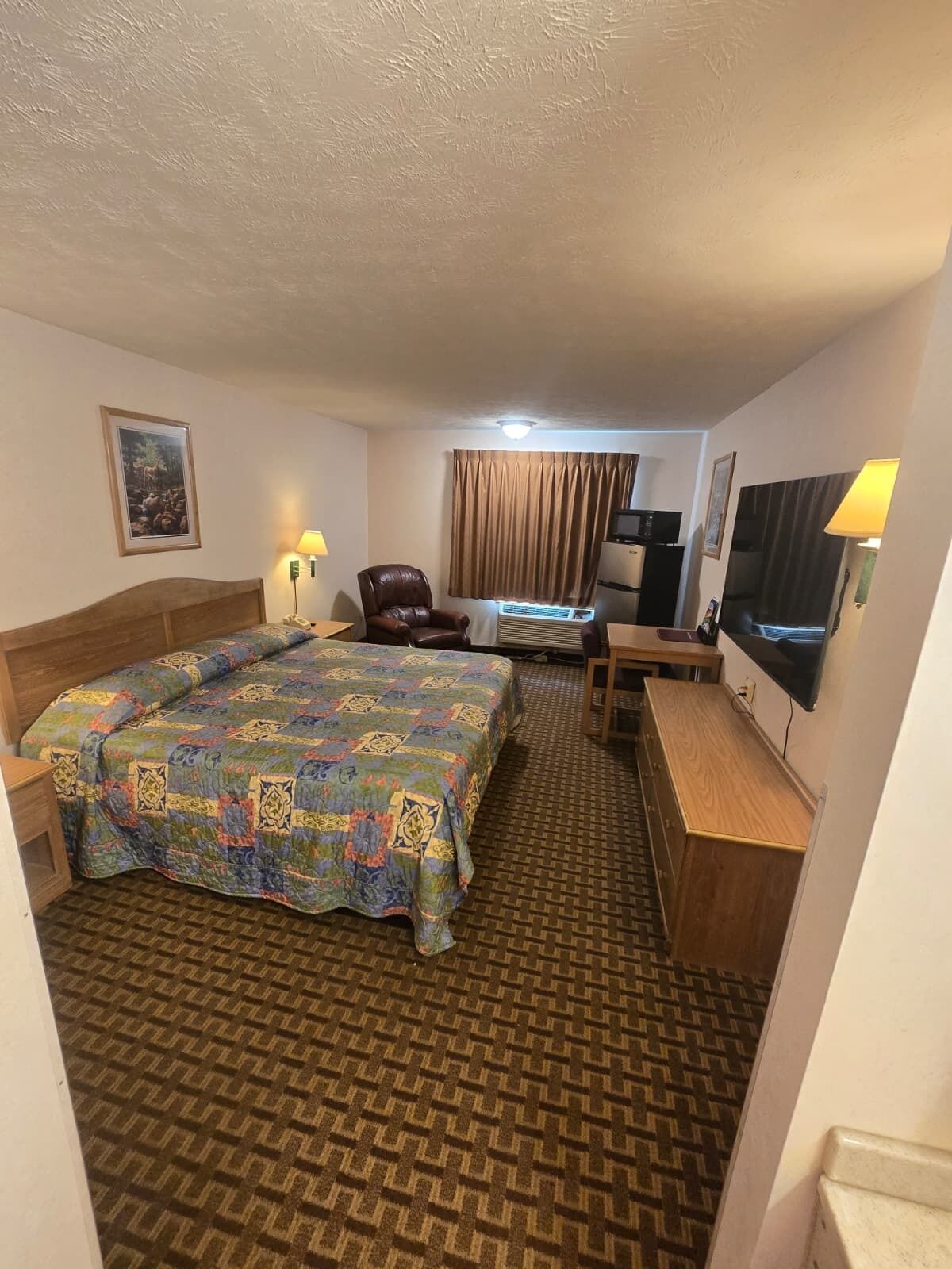 A hotel room with a large bed, a desk, a chair, a television, and a window with curtains.