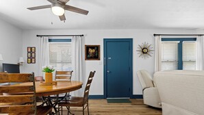 A dining area with a wooden table and chairs, a ceiling fan, and a blue door.