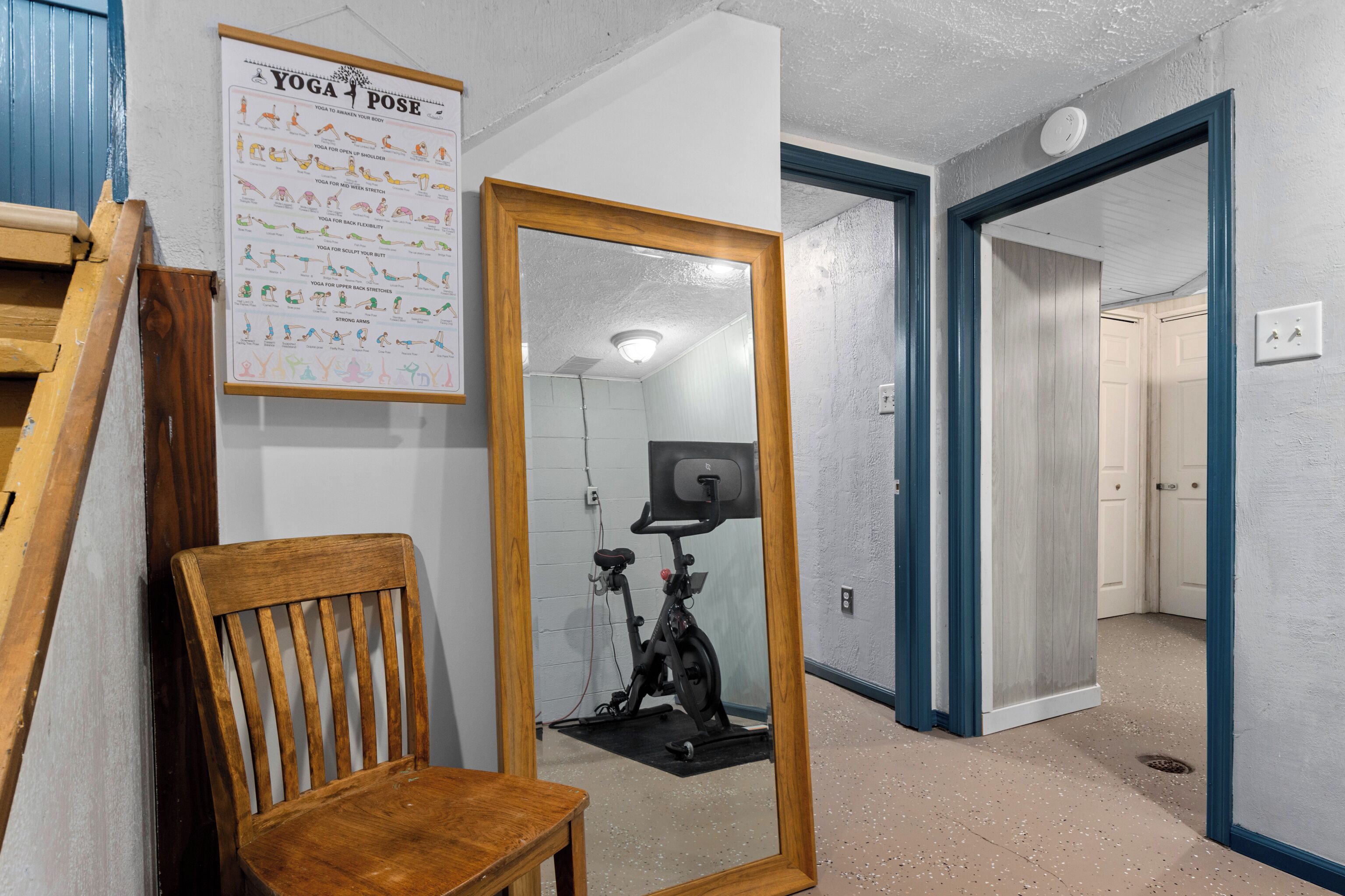 A room with a wooden chair, a mirror, and a yoga poster on the wall.
