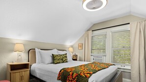 A bedroom with a bed, nightstands, a lamp, a window with blinds, and a view of the outdoors.