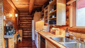 A wooden log cabin kitchen with a central island, built-in shelves, and a large window.