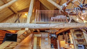 A rustic wooden cabin with a loft bedroom, a kitchen area, and a dining space.