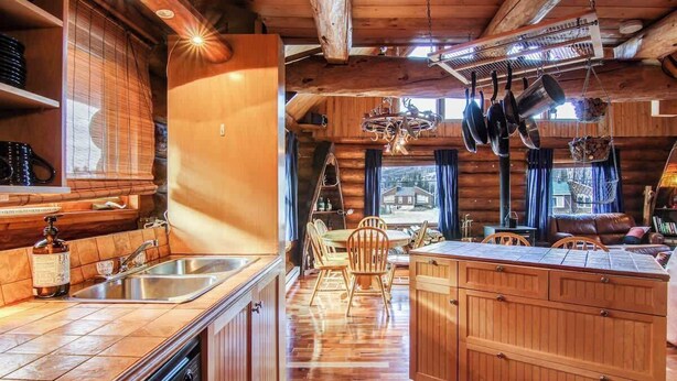 A rustic cabin interior with a wooden dining area, a kitchen with a dishwasher, and a large wooden cabinet.