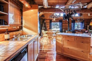 Interior rústico de una cabaña con comedor de madera, cocina con lavavajillas y un gran armario de madera.