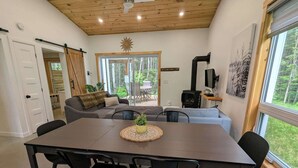 A modern living room with a wooden ceiling, a dining table with chairs, a sofa, and a fireplace.