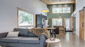 A modern living room with a grey sofa, a small round table, and a kitchen area in the background.