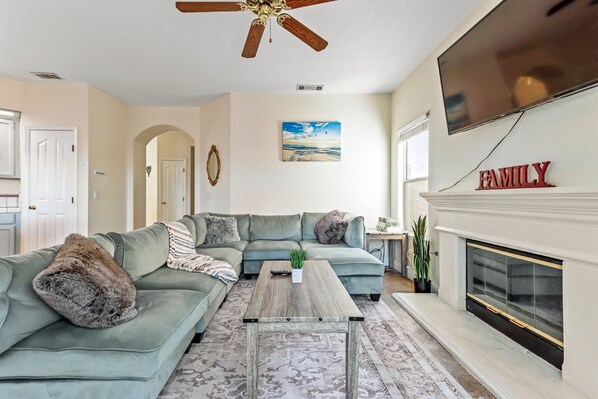 A living room with a sectional sofa, a coffee table, a fireplace, and a ceiling fan.