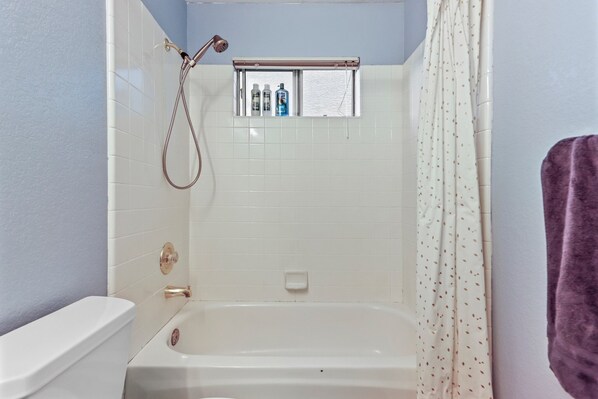 A bathroom with a bathtub, a shower, and a window with toiletries. - Spacious 5BD 3BR Home with Pool table & Air hockey table in Safe Neighborhood (Elk Grove)