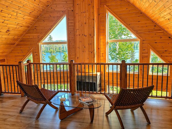 A wooden cabin with a balcony, two wicker chairs, a glass coffee table, and a fireplace.