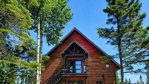 A log cabin with a balcony, a front door, and a staircase leading to the entrance.