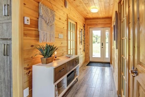 A wooden interior with a white console table, a plant, and a door leading outside.