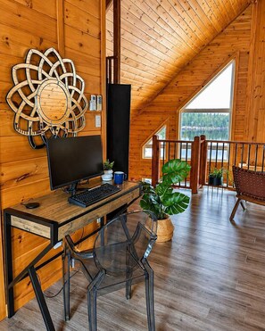 A wooden interior with a computer desk, chairs, a large window, and a view of a lake.