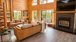 A wooden cabin interior with a sofa, TV, fireplace, and large windows.
