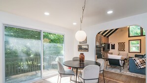 A modern living room with a dining area, large sliding glass doors, and a kitchen visible through an archway.