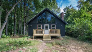 A cabin with a wooden deck, a front door, and a chimney.