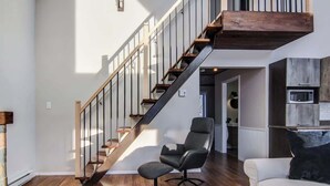 A modern interior with a wooden staircase, a grey armchair, and a white sofa.