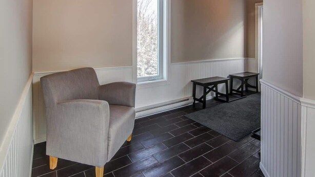 Una habitación con un sillón gris, una mesita, un ventanal con vistas a árboles y suelo de madera oscura.